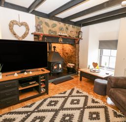 A living room with a television on a stand near a fireplace and a sofa at Buarthau Cottage in Llanrug