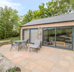 An outdoor patio with a table four chairs and a lounge chair outside a stone building with large sliding glass doors at Coal Drops in Alnwick