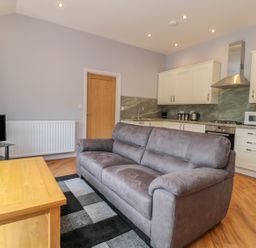A living room with a grey sofa wooden coffee table and kitchen cabinets at Coal Drops in Alnwick