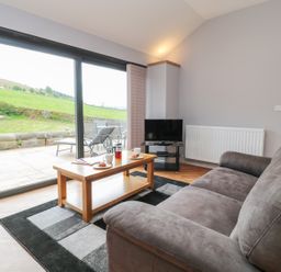 A living room with a gray sofa a wooden coffee table a television and large sliding glass doors at Coal Drops in Alnwick