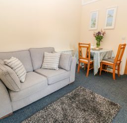 A living room with a grey sofa and pillows a small table with chairs flowers and paintings on the wall at The Old Cows House in Helston