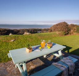 A picnic table with a pitcher of orange drink apples plants and magazines in a garden overlooking the sea at Allt y Mor in Harlech
