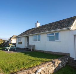 A white house with a stone roof in a garden with a picnic table and wooden bench at Allt y Mor in Harlech