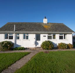 A white single-story house with a tiled roof and three bushes in front at Allt y Mor in Harlech