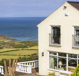 A house with white walls and black railings near the coast with green fields and a body of water at Amolca in Llaneilian