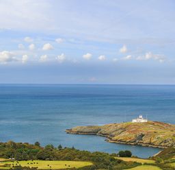 A coastal landscape with a lighthouse on a small peninsula surrounded by the sea and fields at Amolca in Llaneilian