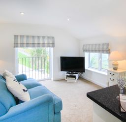 A living room with a blue sofa two windows with striped blinds a television on a stand two lamps a bottle of wine glasses and a box of chocolates at Amolca in Llaneilian