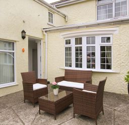 An outdoor patio with four wicker chairs and a glass table with a flower pot at Amolca in Llaneilian