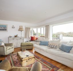 A living room with beige sofas armchairs a patterned rug wooden floor and large windows at Angorfa - Trearddur Bay in Trearddur Bay
