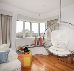 A living room with a hanging bubble chair and a curved bench by the window at Angorfa - Trearddur Bay