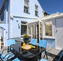 An outdoor patio with a glass table and six blue chairs next to a light blue house at Arkoo Rhosneigr