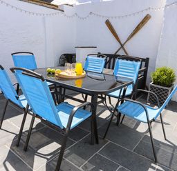 An outdoor patio area with a black glass table surrounded by six blue chairs and a black bench at Arkoo in Rhosneigr