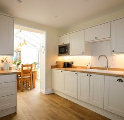 A kitchen with white cabinets wooden countertops and a dining area with wooden chairs at Arkoo in Rhosneigr