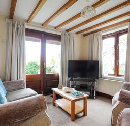 A living room with sofas a wooden coffee table a television and a door with windows at Barras Cottage in Brynsiencyn