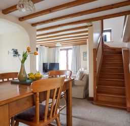 A dining area with wooden table and chairs adjacent to a living room with sofa and television at Barras Cottage in Brynsiencyn