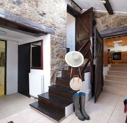 An entryway with stone walls showing stairs leading to a kitchen a black door a bathroom and a hat stand with boots and hats at Foel Stable Cottage Brynsiencyn