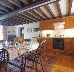 A kitchen with wooden cabinets a dining table set for breakfast and chairs at Foel Stable Cottage in Brynsiencyn