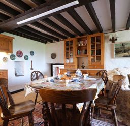 A dining area with a wooden table set for breakfast surrounded by wooden chairs and a bookshelf at Foel Stable Cottage in Brynsiencyn