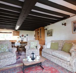 A sitting area with floral patterned armchairs and sofa a wooden coffee table with cups and plates and a dining table in the background at Foel Stable Cottage in Brynsiencyn