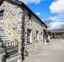 An outdoor view of a stone building with stairs and a gate next to a paved area with plants at Bryn Eira Stables in Llanfair PG