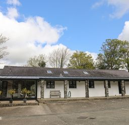 An exterior view of a stone and white painted building with multiple windows and a bench outside at Bryn Eira Stables in Llanfair PG