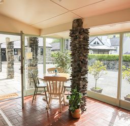 A dining area with a round table and four chairs next to stone pillars and large windows at Bryn Eira Stables Llanfair PG