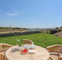 An outdoor wooden table with chairs bowls of strawberries and meringues set on a lawn with a stone wall and water view at Bwthyn Glanrhyd in Llanfair yn Neubwll