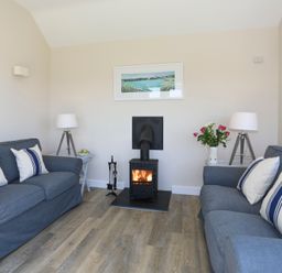 A living room with two blue sofas white cushions a wood burning stove and two lamps at Bwthyn Glanrhyd in Llanfair yn Neubwll