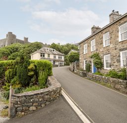 A street with stone houses and a castle on a hill in the background at Bron Castell in Harlech
