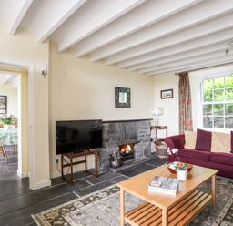 A living room with a maroon sofa a wooden coffee table a television a stone fireplace and a window with curtains at Bron Castell in Harlech