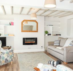 A living room with a sofa an armchair a wall-mounted electric fireplace and shelves at Brook Cottage in Criccieth