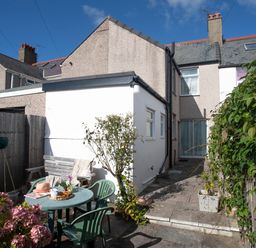 A small patio with a round table and chairs outside a house with a white extension at Bro Dawel in Beaumaris