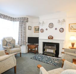 A living room with armchairs a fireplace and a television at Bro Dawel in Beaumaris