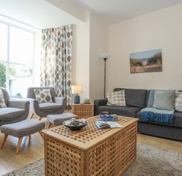 A living room with two armchairs and a sofa with cushions a wooden coffee table and a side table with a lamp and a floor lamp at Bryn Dale in Trearddur Bay