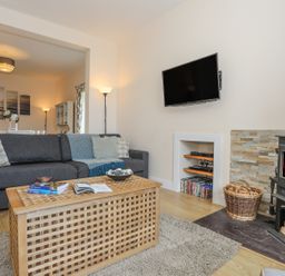 A living room with a grey sofa a wooden coffee table a wood burning stove and a wall mounted TV at Bryn Dale in Trearddur Bay