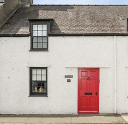 A white house exterior with black window frames and a red door at Bryn Tegid in Beaumaris