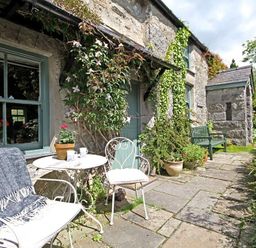 A stone cottage exterior with a small patio table and chairs plants and a green bench at Buck Cottage in Red Wharf Bay