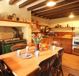 A kitchen with a wooden dining table and chairs a stove flowers on the table and wooden cabinets at Buck Cottage in Red Wharf Bay