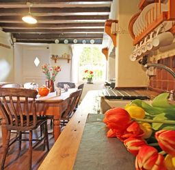 A kitchen with a wooden dining table and chairs and flowers on the counter at Buck Cottage in Red Wharf Bay