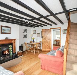 A living room with a fireplace wooden dining table chairs and carpeted stairs at Cae Person in Llangoed