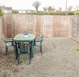 An outdoor area with a plastic table and four chairs on gravel near a wooden fence at Cae Person in Llangoed