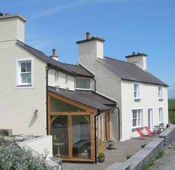 A white two-story house with multiple chimneys and a glass extension on a gravel driveway in a rural area at Cae'r Dyni Criccieth