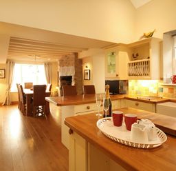 A kitchen with wooden countertops a dining table with chairs and a stone fireplace at Cae'r Dyni (Caer Dyni) in Criccieth