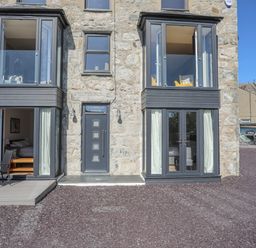 Stone building exterior with two bay windows a central door labeled Cambrian House and outdoor seating at Cambrian House in Criccieth