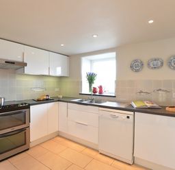 A kitchen with white cabinets a dishwasher an oven and a window with flowers on the sill at Cefn Isaf in Porthmadog