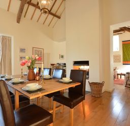 A dining room with a wooden table set with plates bowls candlesticks and flowers next to a fireplace and a sitting area visible through an open doorway at Cefn Isaf in Porthmadog