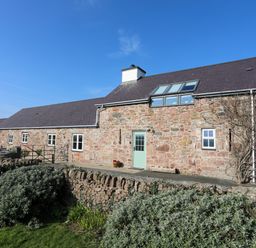 A stone cottage with a slate roof and garden in front at Tan Twr - Chellow Cottage in Dwyran