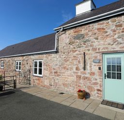 Stone cottage exterior with light green door and windows with flower pot at Tan Twr - Chellow Cottage in Dwyran
