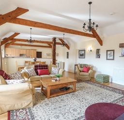 A living room with beige sofas wooden coffee table dining area and exposed wooden beams at Tan Twr - Chellow Cottage in Dwyran