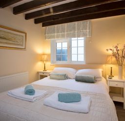 A bedroom with a double bed with rolled towels on it two bedside tables with lamps and a window at The Coach House - Beaumaris